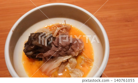 close up of Japanese Sukiyaki hot pot wagyu beef slice, mushroom (enoki) and cabbage in a rich orange raw egg yolk broth sauce in a white bowl on a wooden table with copy space close up of Japanese Sukiyaki hot pot wagyu beef slice, mushroom (enoki) and cabbage in a rich orange raw egg yolk broth sauce in a white bowl on a wooden table with copy space 140761055