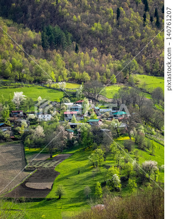 Lush green hills frame a quiet village below, vertical view. Lush green hills frame a quiet village below, vertical view. 140761207