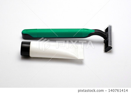 Green razor rests beside white tube on clean white surface. Minimalist setup highlights grooming essentials clearly. Ideal for beauty or personal care product advertisements Green razor rests beside white tube on clean white surface. Minimalist setup highlights grooming essentials clearly. Ideal for beauty or personal care product advertisements 140761414
