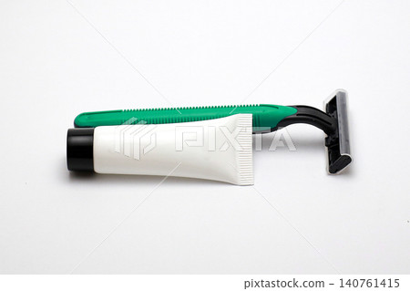 Green razor rests beside white tube on clean white surface. Minimalist setup highlights grooming essentials clearly. Ideal for beauty or personal care product advertisements Green razor rests beside white tube on clean white surface. Minimalist setup highlights grooming essentials clearly. Ideal for beauty or personal care product advertisements 140761415