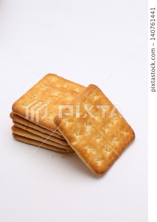 Golden crackers rest on plain white surface. Stacked neatly, one leans forward slightly. Crumbly texture shows crisp, baked perfection. Ideal for food, snack, or bakery promotional 140761441