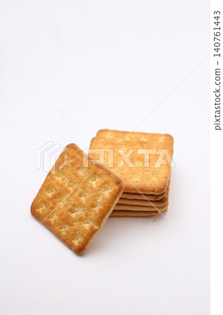 Golden crackers rest on plain white surface. Stacked neatly, one leans forward slightly. Crumbly texture shows crisp, baked perfection. Ideal for food, snack, or bakery promotional Golden crackers rest on plain white surface. Stacked neatly, one leans forward slightly. Crumbly texture shows crisp, baked perfection. Ideal for food, snack, or bakery promotional 140761443