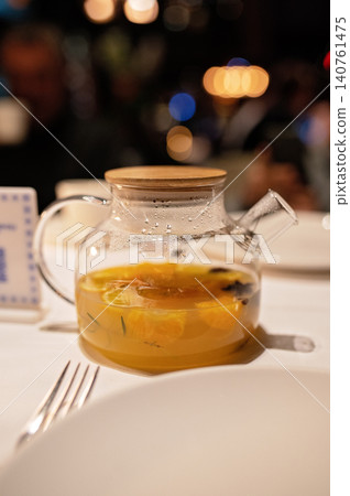 Glass teapot with citrus fruit infusion on table in restaurant setting with blurred background 140761475
