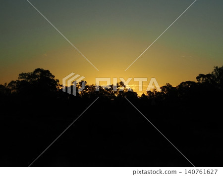 The sunset sky illuminates the silhouettes of the trees in the view from the train window—a gentle light envelops the journey. 140761627