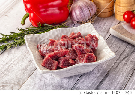 Raw beef cubes in white bowl with red pepper garlic and rosemary on wooden table Raw beef cubes in white bowl with red pepper garlic and rosemary on wooden table 140761746