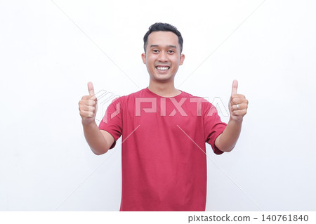 Young man wears red tshirt. He smiles broadly with joy and enthusiasm. Both hands form OK gestures, showing approval. Simple white background enhances focus on his expression Young man wears red tshirt. He smiles broadly with joy and enthusiasm. Both hands form OK gestures, showing approval. Simple white background enhances focus on his expression 140761840