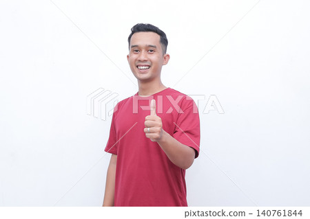 Young man wears red t-shirt. He smiles broadly with joy and enthusiasm. Both hands form OK gestures, showing approval. Simple white background enhances focus on his expression Young man wears red t-shirt. He smiles broadly with joy and enthusiasm. Both hands form OK gestures, showing approval. Simple white background enhances focus on his expression 140761844