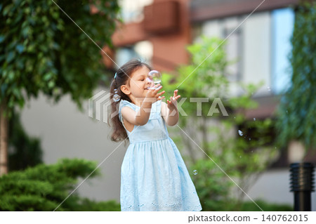 Young child laughing, playing with soap bubbles outside, enjoying childhood innocence in a blue dress Young child laughing, playing with soap bubbles outside, enjoying childhood innocence in a blue dress 140762015