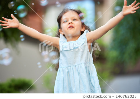 Happy little child playing with soap bubbles in outdoors. Joyful kid enjoying summer playtime activity on a sunny day 140762023