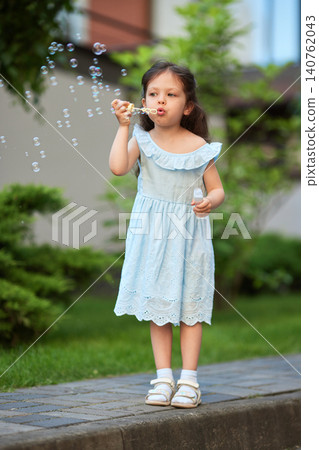 Child blowing soap bubbles in an outdoor setting, capturing innocence, joy, and playful activity during summer 140762043