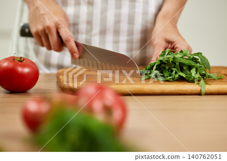 Woman's hands preparing fresh healthy ingredients with a knife on a cutting board, making a salad in the kitchen 140762051