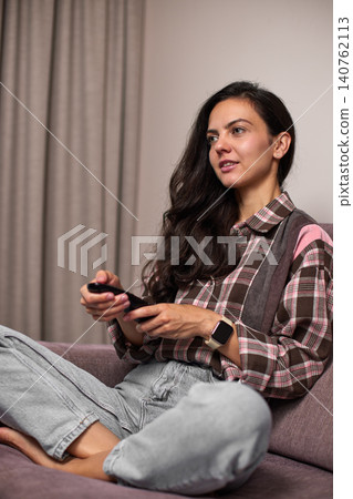 Woman sitting on sofa holding remote control, changing channels, enjoying leisure time, lifestyle concept 140762113