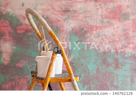 DIY home renovation scene featuring paint-splattered yellow step ladder with paint buckets and wooden mixing stick against colorful textured wall. Interior remodeling, decorating concept copy space 140762126