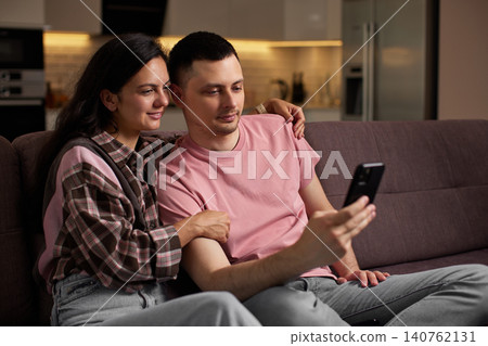 Young couple enjoying leisure time on sofa at home, streaming content or browsing social media on a mobile phone 140762131