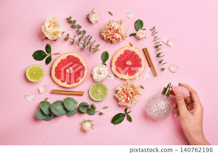 Top view of woman spraying perfume on pink background, flowers and citrus fruits representing aroma 140762198