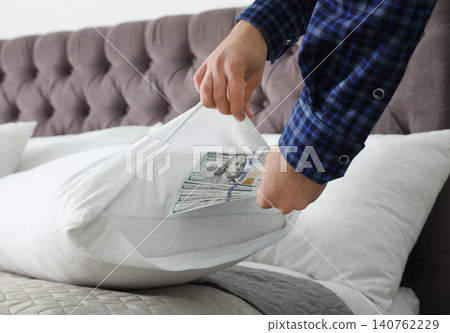 Man hiding dollar banknotes in pillow case indoors, closeup. Money savings Man hiding dollar banknotes in pillow case indoors, closeup. Money savings 140762229
