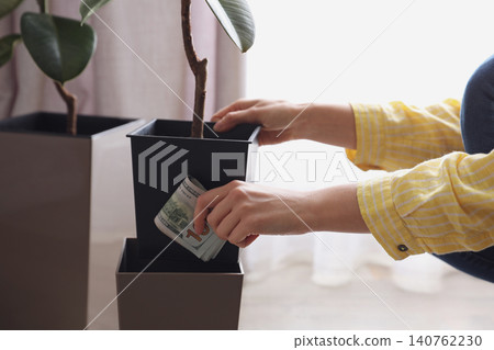 Woman hiding dollar banknotes in flower pot indoors, closeup. Money savings Woman hiding dollar banknotes in flower pot indoors, closeup. Money savings 140762230
