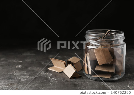 Glass jar with paper pieces on grey table, space for text Glass jar with paper pieces on grey table, space for text 140762290