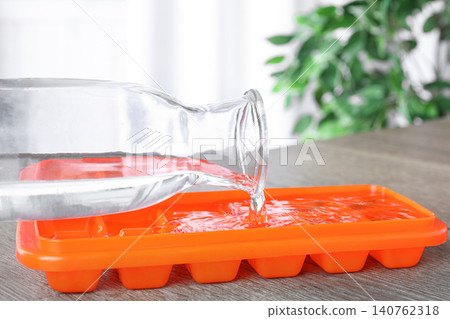 Pouring water into ice cube tray on wooden table, closeup Pouring water into ice cube tray on wooden table, closeup 140762318