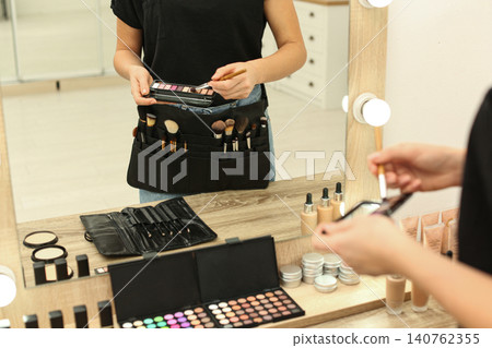 Professional makeup artist with eyeshadow palette and belt organizer full of tools in studio, closeup Professional makeup artist with eyeshadow palette and belt organizer full of tools in studio, closeup 140762355