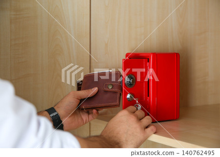 Man putting wallet into small red steel safe, closeup Man putting wallet into small red steel safe, closeup 140762495