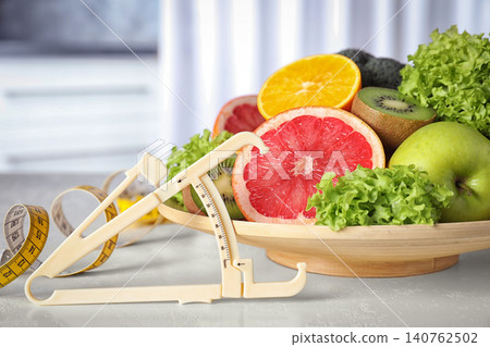 Body fat caliper, measuring tape, vegetables and fruits on table. Diet plan from nutritionist Body fat caliper, measuring tape, vegetables and fruits on table. Diet plan from nutritionist 140762502
