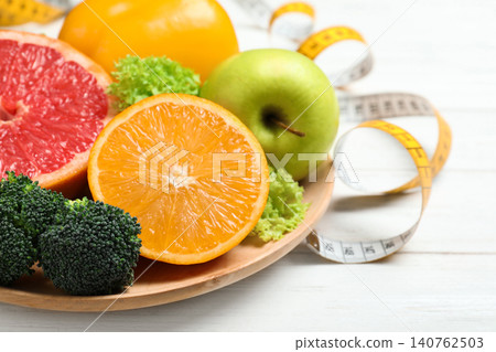 Fruits, vegetables and measuring tape on white wooden background, closeup. Visiting nutritionist 140762503