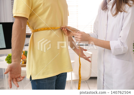 Young nutritionist measuring patient's waist in clinic, closeup Young nutritionist measuring patient's waist in clinic, closeup 140762504