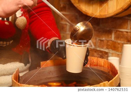 Seller pouring tasty aromatic mulled wine into cup at winter fair, closeup 140762531