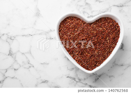 Brown rice in heart shaped bowl on white marble table, top view. Space for text Brown rice in heart shaped bowl on white marble table, top view. Space for text 140762568