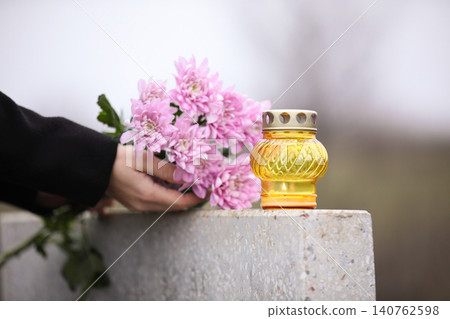 Woman holding chrysanthemum flowers near grey granite tombstone with candle outdoors, closeup. Funeral ceremony Woman holding chrysanthemum flowers near grey granite tombstone with candle outdoors, closeup. Funeral ceremony 140762598