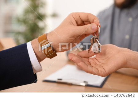 Real estate agent giving key with trinket to client in office, closeup Real estate agent giving key with trinket to client in office, closeup 140762648