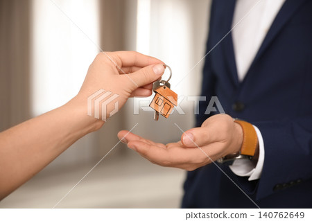 Real estate agent giving key with trinket to client in office, closeup Real estate agent giving key with trinket to client in office, closeup 140762649