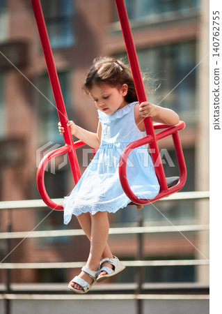Child enjoying playtime on a playground swing. Innocence and joy during childhood summer outdoor activities Child enjoying playtime on a playground swing. Innocence and joy during childhood summer outdoor activities 140762755