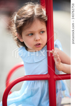 Child girl is swinging on a red swing set, enjoying childhood during summer 140762758