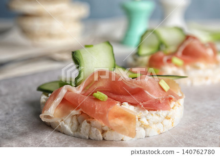 Puffed rice cake with prosciutto and cucumber on parchment paper, closeup Puffed rice cake with prosciutto and cucumber on parchment paper, closeup 140762780
