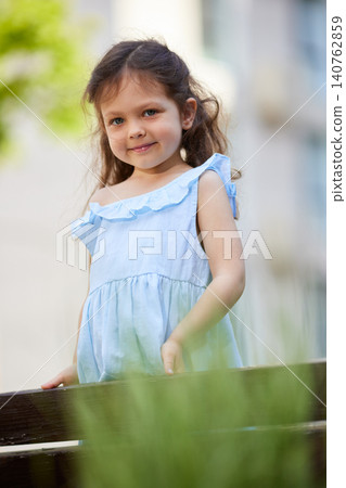 Cute girl with brown hair and blue eyes wearing a light blue dress. Posing and smiling in a park setting Cute girl with brown hair and blue eyes wearing a light blue dress. Posing and smiling in a park setting 140762859