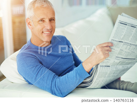 Senior, man and portrait with newspaper on sofa for article, information and morning routine in living room of home. Elderly, person and face with media story for global news, smile or relax on couch 140763116