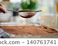 Hand holds sieve over tiramisu dessert covered with cocoa powder 140763741