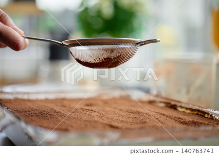 Hand holds sieve over tiramisu dessert covered with cocoa powder 140763741
