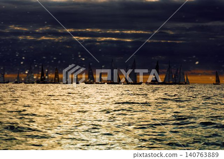 A lot of sailing boats through splashing water at sunset, Sailing regatta in the Gulf of Finland at sunset, hot race of several yachts, teamwork A lot of sailing boats through splashing water at sunset, Sailing regatta in the Gulf of Finland at sunset, hot race of several yachts, teamwork 140763889
