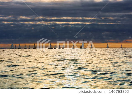 A lot of sailing boats through splashing water at sunset, Sailing regatta in the Gulf of Finland at sunset, hot race of several yachts, teamwork A lot of sailing boats through splashing water at sunset, Sailing regatta in the Gulf of Finland at sunset, hot race of several yachts, teamwork 140763893