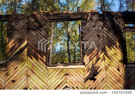 A stark contrast: charred wood from a fire-ravaged building framing a vibrant glimpse of nature and a clear sky beyond A stark contrast: charred wood from a fire-ravaged building framing a vibrant glimpse of nature and a clear sky beyond 140763999