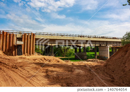 Concrete bridge under construction amidst a dirt-filled site on a sunny spring day, showing ongoing infrastructure development 140764054