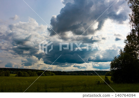 Moody summer sky with dramatic, heavy clouds gathering over a vibrant green field and distant forest. A powerful nature vista Moody summer sky with dramatic, heavy clouds gathering over a vibrant green field and distant forest. A powerful nature vista 140764094