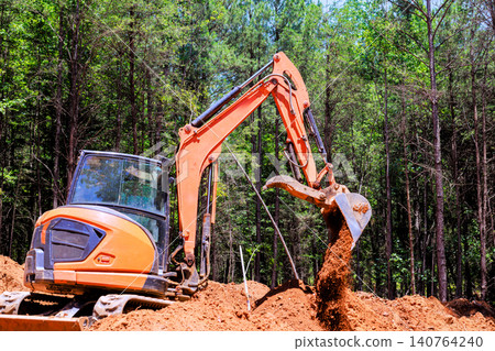 Excavator is working in forested area, moving dirt during digging trenches construction project Excavator is working in forested area, moving dirt during digging trenches construction project 140764240