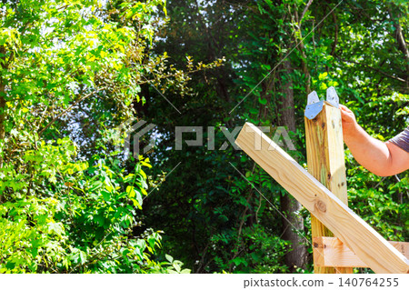 Contractor is building wooden beams frame using lumber metal brackets in construction works area Contractor is building wooden beams frame using lumber metal brackets in construction works area 140764255