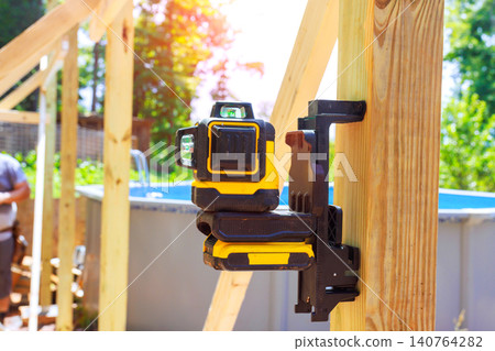 Laser level tool is mounted on wood at construction site where workers are framing building outdoors. Laser level tool is mounted on wood at construction site where workers are framing building outdoors. 140764282
