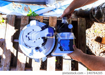 Worker connects parts of pool filter pump near swimming pool while working outside on sunny day. Worker connects parts of pool filter pump near swimming pool while working outside on sunny day. 140764285