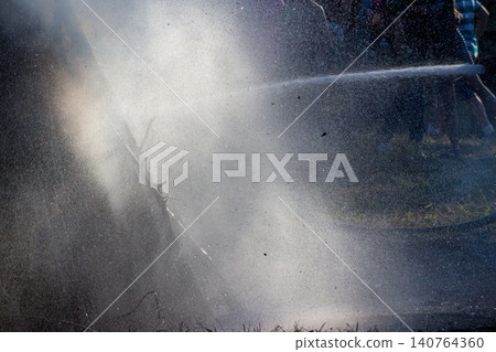 Powerful jet of water extinguishing a glowing bonfire during a summer folk festival, spraying droplets and mist creating a dramatic contrast between hot embers and cool moisture Powerful jet of water extinguishing a glowing bonfire during a summer folk festival, spraying droplets and mist creating a dramatic contrast between hot embers and cool moisture 140764360